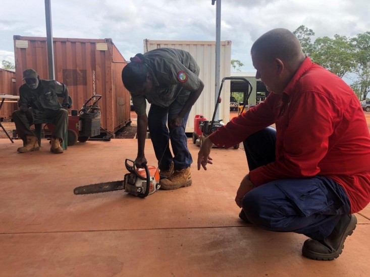 Train Safe NT's Ian van Munster showing Florence Biridjala how to use a chainsaw, with Peter Djigirr looking on